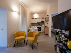 Un salon moderne avec deux fauteuils jaunes, un téléviseur à écran plat et une bibliothèque contenant des livres et des objets décoratifs.