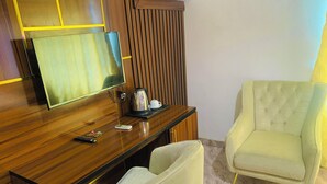 A hotel room with a wooden desk, a television, a coffee maker, and a light-colored armchair. - Vienna International Hotel (Asaba)