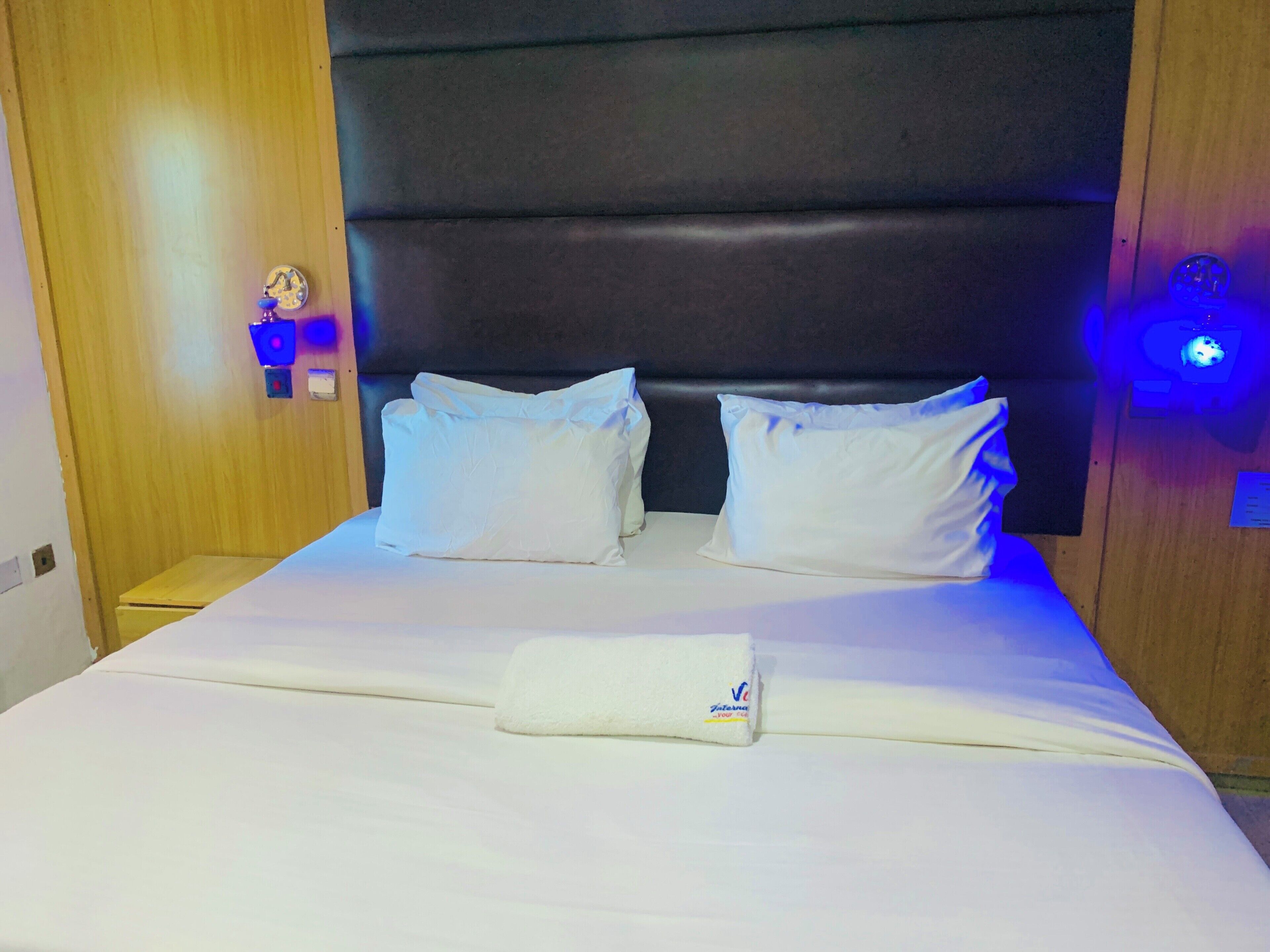 Una camera d'albergo con un letto grande, due cuscini, un asciugamano piegato con cura e una testiera con illuminazione integrata.