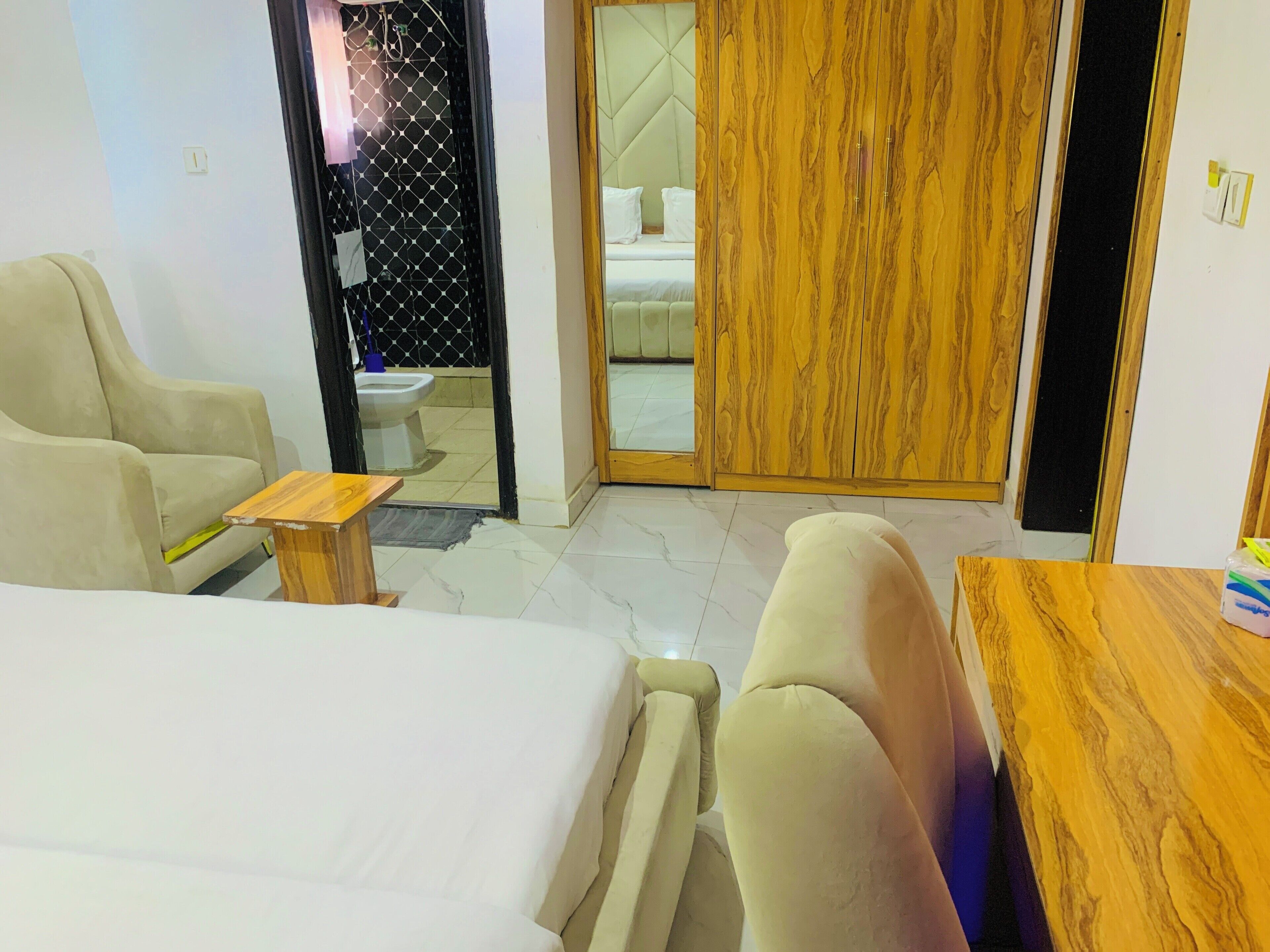 A hotel room with a bed, a sofa, a wooden side table, and a bathroom visible through an open door.