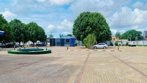 A paved parking area with trees, a blue building, and a white car. - Vienna International Hotel (Asaba)