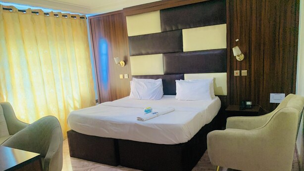 A hotel room with a large bed, two armchairs, a desk, and a nightstand. - Vienna International Hotel (Asaba)