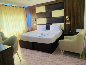A hotel room with a large bed, two armchairs, a desk, and a nightstand. - Vienna International Hotel (Asaba)