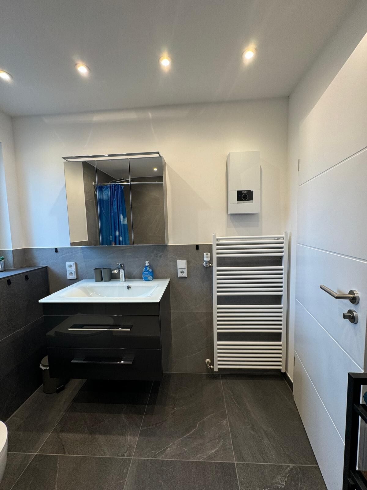 Uma casa de banho moderna com uma grande pia, azulejos escuros, um porta-toalhas e um cabine de duche.