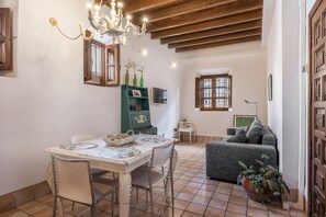 Un comedor con una mesa y sillas, una araña, un armario verde con objetos decorativos, un sofá gris y una planta en maceta.