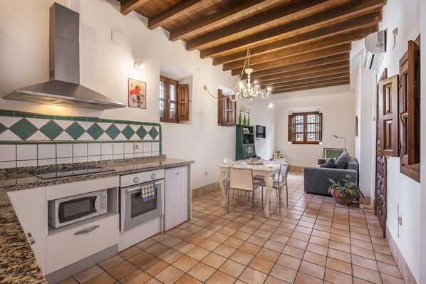 Una cocina con horno empotrado, microondas y campana extractora de acero inoxidable. Hay un comedor con mesa y sillas, y una sala de estar con sofá y una planta en maceta.