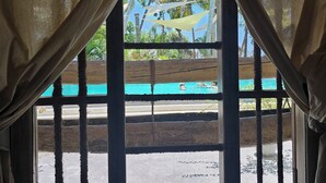 A room with a view of a swimming pool and palm trees through a window with a wooden frame and metal bars. - Deep Blue Sea Rental Villa (Matara)