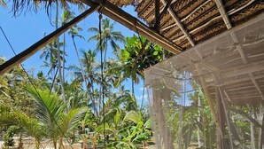 A hammock under a thatched roof structure with a view of palm trees and a sandy ground. - Deep Blue Sea Rental Villa (Matara)