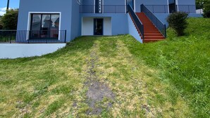 A modern two-story house with a red staircase, a covered porch, and a grassy yard. - Blue Almance - T2 Apartment (São João)