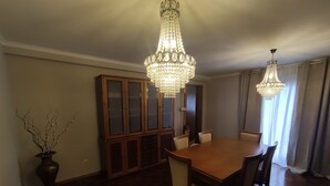 A dining area with a wooden table and chairs, a chandelier, and a cabinet with glass doors. - Blue Almance - T2 Apartment (São João)