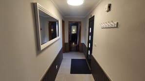 A hallway with a mirrored wall, a black mat at the entrance, and a ceiling light. - Blue Almance - T2 Apartment (São João)