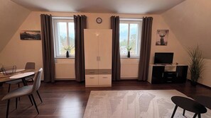 A room with a dining table, chairs, a TV, and a cabinet. - Haus am Röblinsee - Holiday apartment Elster in Fürstenberg / Havel (Fürstenberg/Havel)