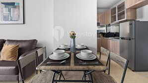 A modern dining area with a wooden table set for six, a brown leather couch, and a kitchen with stainless steel appliances. - Averona by Kozystay - Taman Sari (Jakarta)