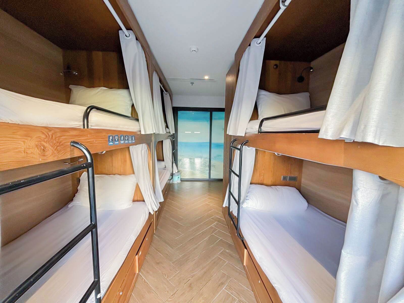 A narrow corridor with bunk beds on either side, wooden walls, and a view of the sea through a glass door.