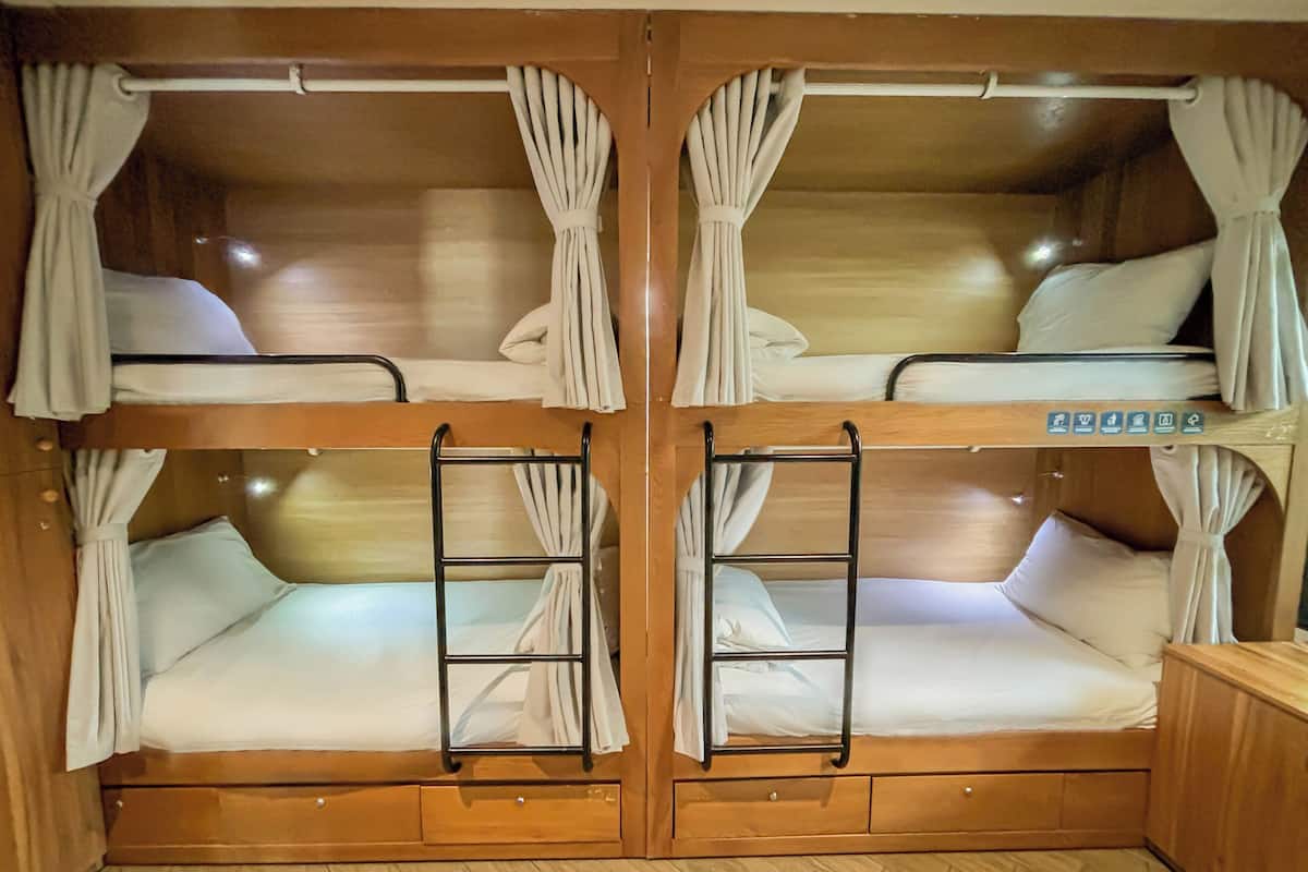 A bunk bed room with curtains, a ladder, and a wooden floor.