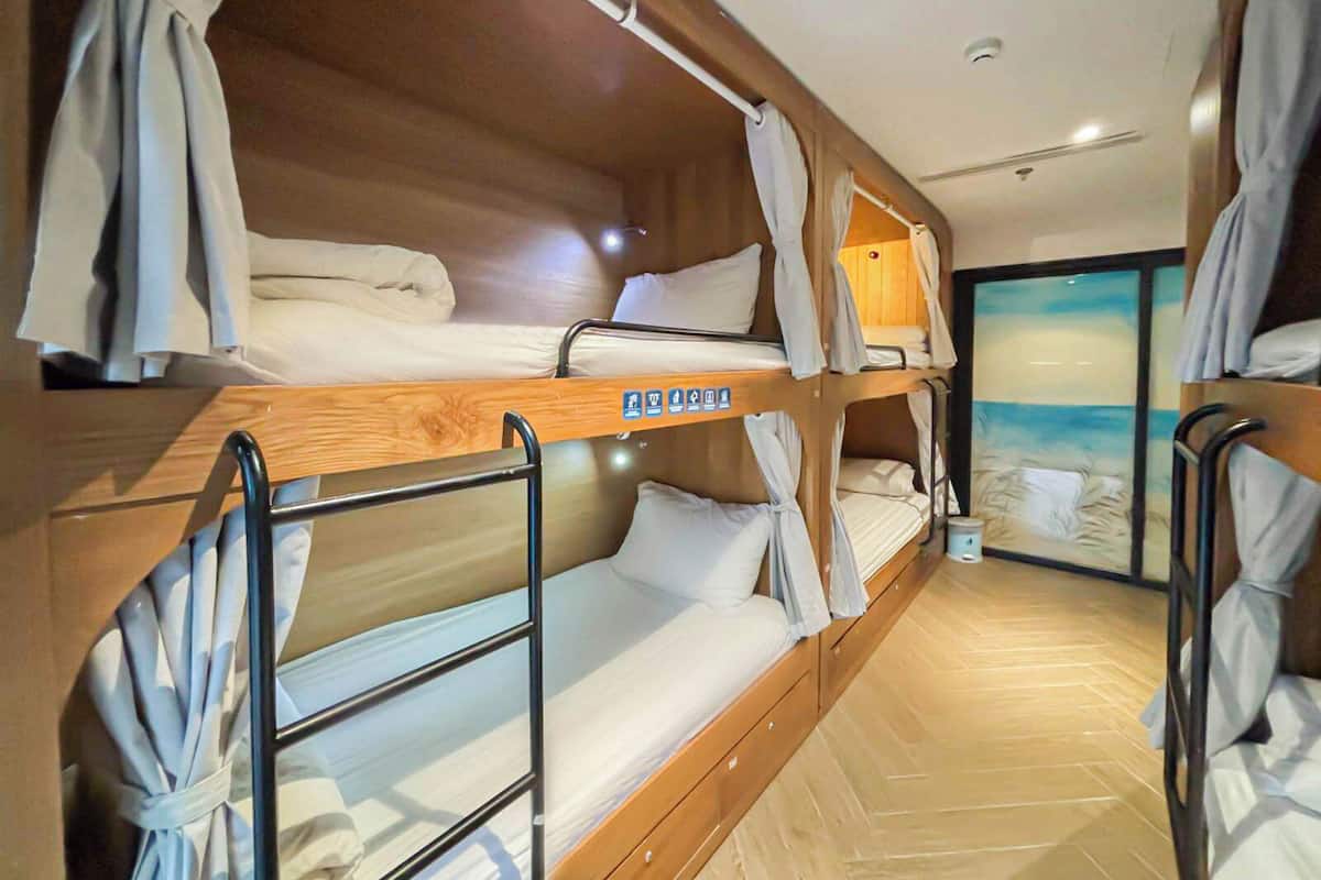 A bunk room with wooden bunk beds, white bedding, and a view of the sea through a large window.