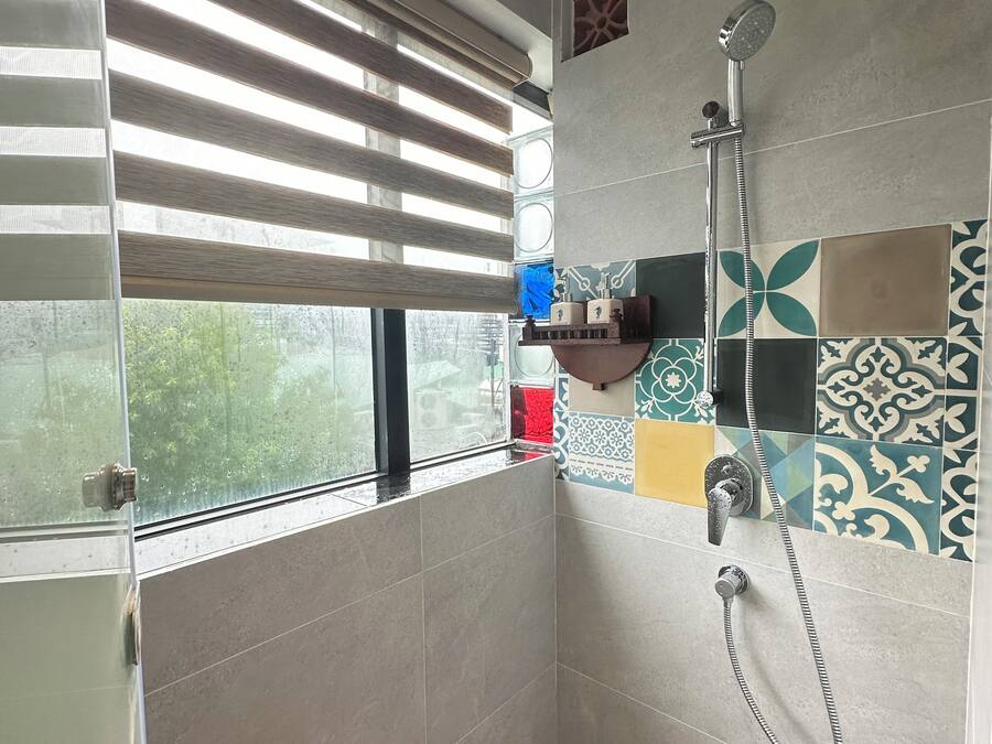 A small, modern bathroom with a shower, a window with blinds, and a tiled wall with a decorative pattern.