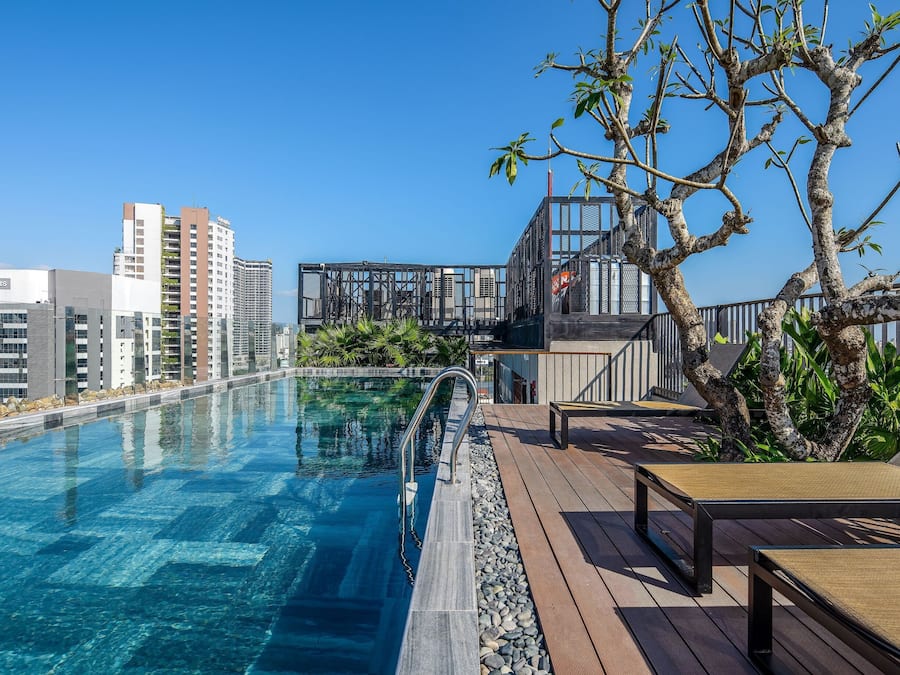 A rooftop pool with clear blue water, wooden deck, and lounge chairs.