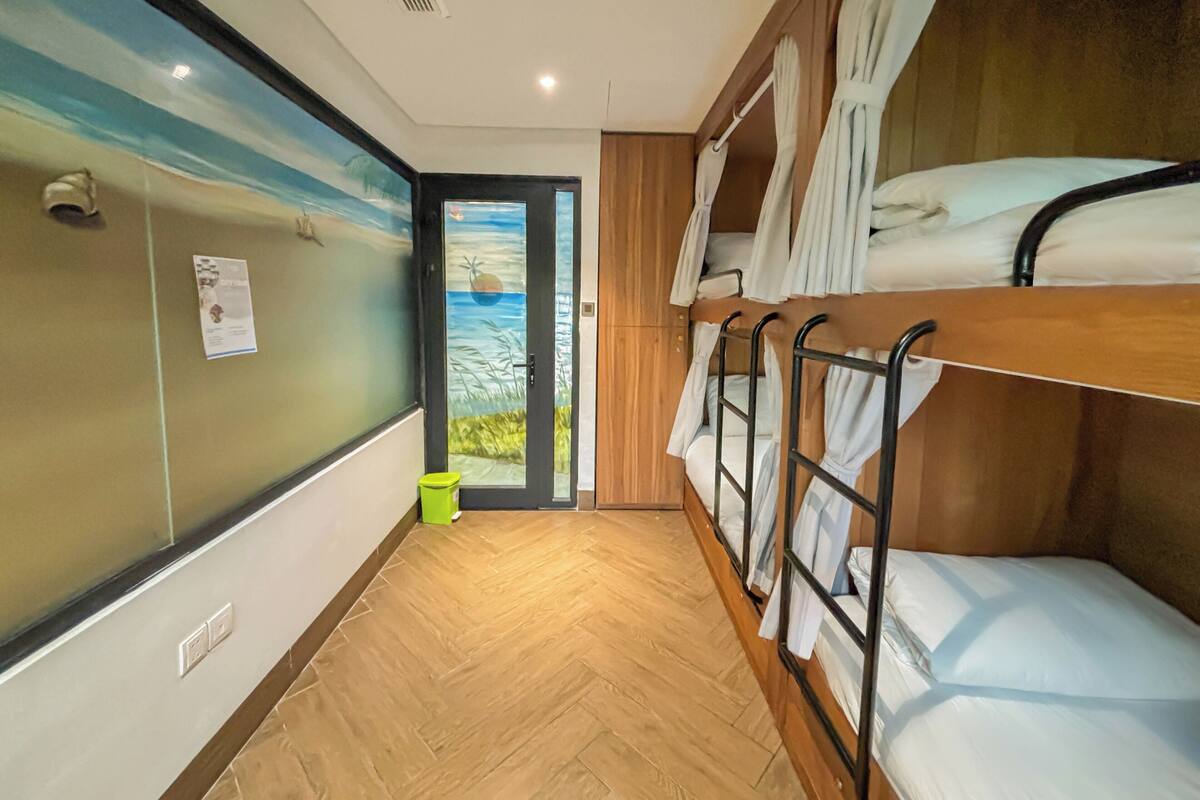 A room with bunk beds, a wooden floor, a beach mural, and a door with a view.