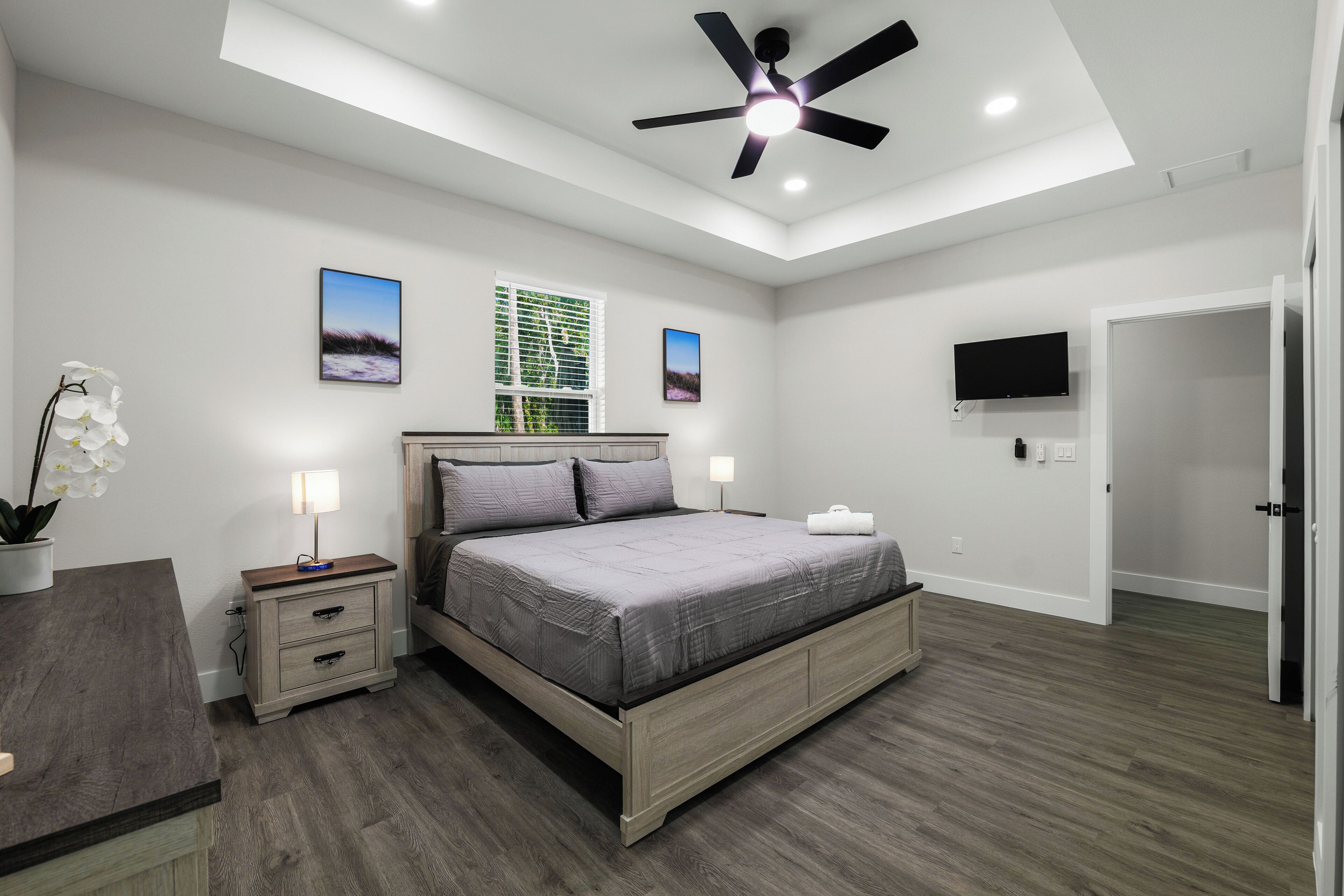 Une chambre à coucher avec un lit, des tables de chevet, un ventilateur de plafond et un téléviseur.