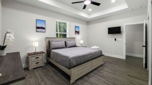 Un dormitorio con cama, mesitas de noche, ventilador de techo y televisión.