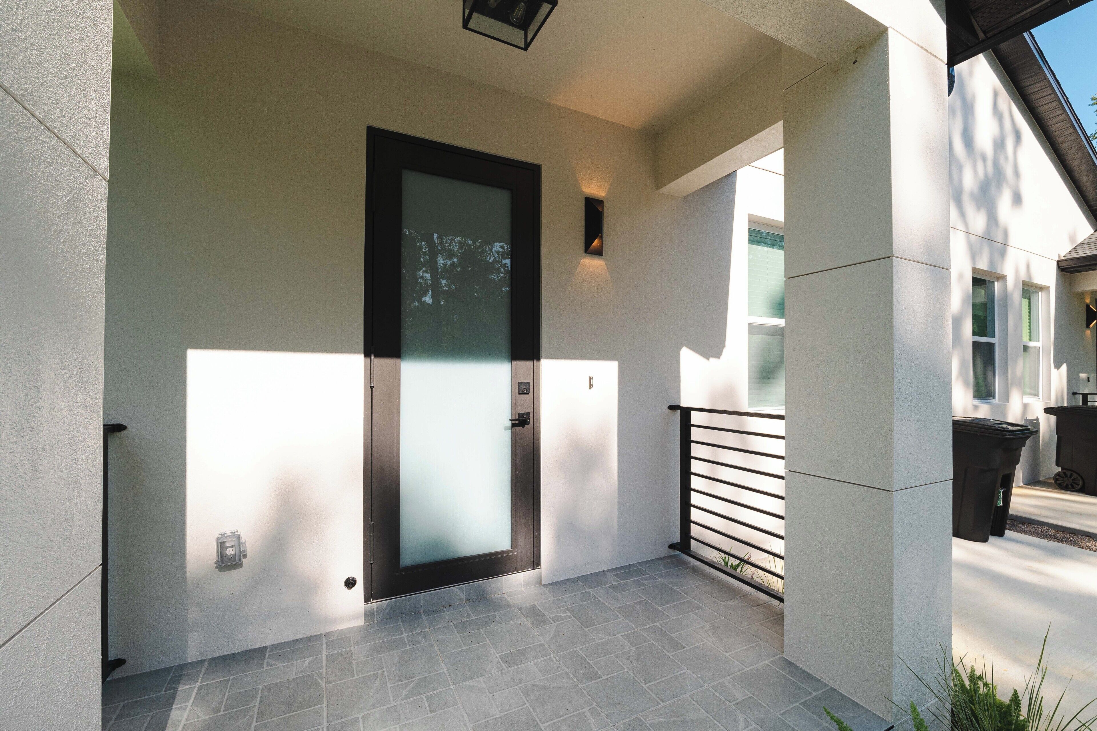 Une façade moderne avec une porte en verre dépoli, une rambarde en métal et un sol carrelé.