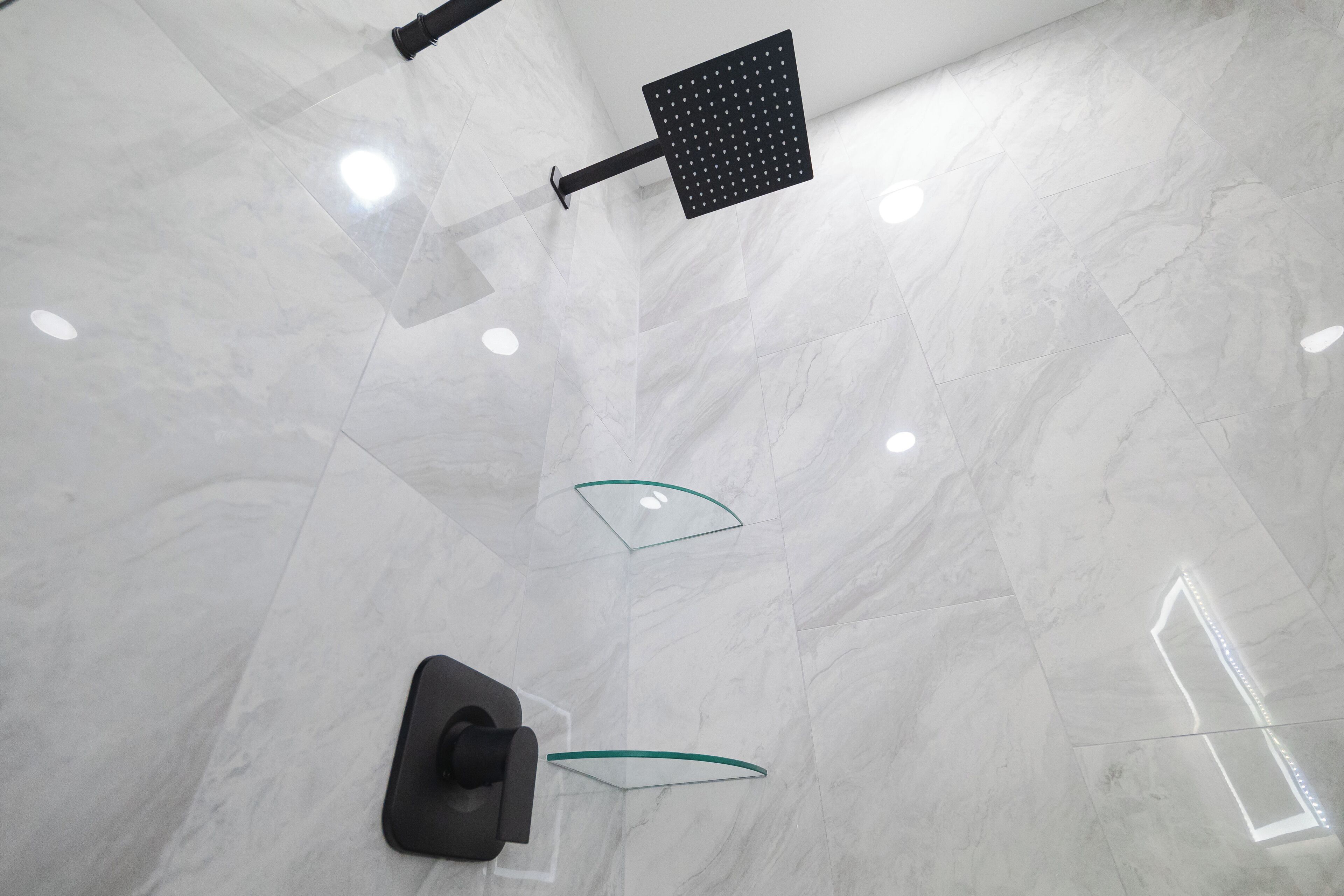 Une salle de bain moderne avec un grand miroir, une pomme de douche et une cabine de douche en verre.