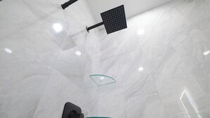 Un baño moderno con un espejo grande, un cabezal de ducha y una mampara de cristal.