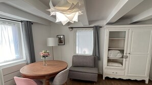 Une pièce comprenant une table ronde en bois, deux chaises, un canapé, un meuble avec des étagères et un luminaire au plafond.