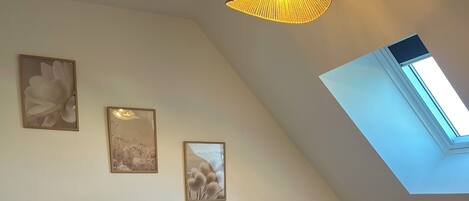 A bedroom with a large bed, a skylight, and three framed pictures on the wall.