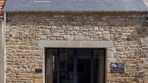 Un edificio de piedra con techo de tejas, una ventana pequeña y una puerta con paneles de vidrio.