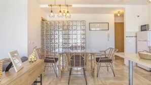 Un espace repas séparé par une cloison en verre, avec des chaises en osier, une table en bois et un luminaire suspendu.
