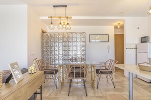 A dining area with a glass partition, wicker chairs, a wooden table, and a hanging light fixture.