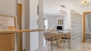 Un intérieur moderne avec un coin repas comprenant une table en verre et des chaises en osier, un meuble en bois et un certificat encadré accroché au mur.