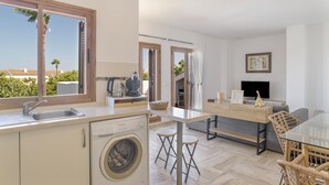 Une cuisine moderne équipée d’un lave-linge, un coin repas avec une table en verre et une vue sur les palmiers.