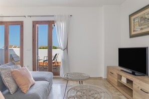A modern living room with a sofa, a glass coffee table, a TV on a wooden stand, and a sliding glass door leading to an outdoor area. - Apartment 'Maracaibo' with Shared Pool, Wi-Fi and Air Conditioning (Novo Sancti Petri)