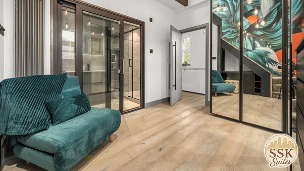 Una sala de estar moderna con un sofá color turquesa, un ventanal de vidrio que da a un balcón y una escalera con un mural.