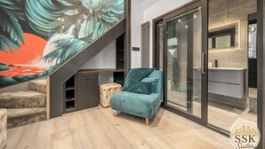 Un interior moderno con una escalera, un sillón verde azulado y una puerta de cristal que da a un baño.