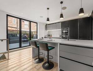 A modern kitchen with a large island, bar stools, pendant lighting, and a view of the outside.