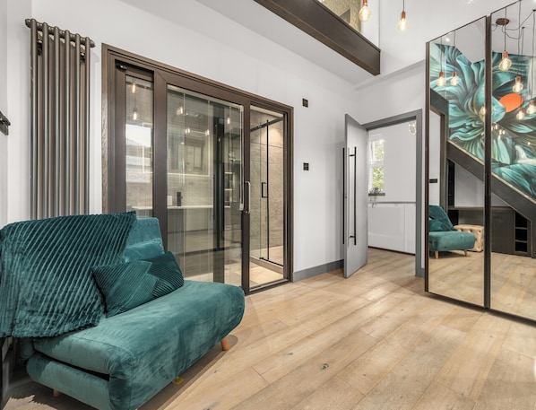 A modern living room with a teal sofa, a glass door leading to a balcony, and a staircase with a mural.