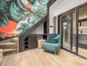 A modern interior with a staircase, a teal armchair, and a glass door leading to a bathroom.