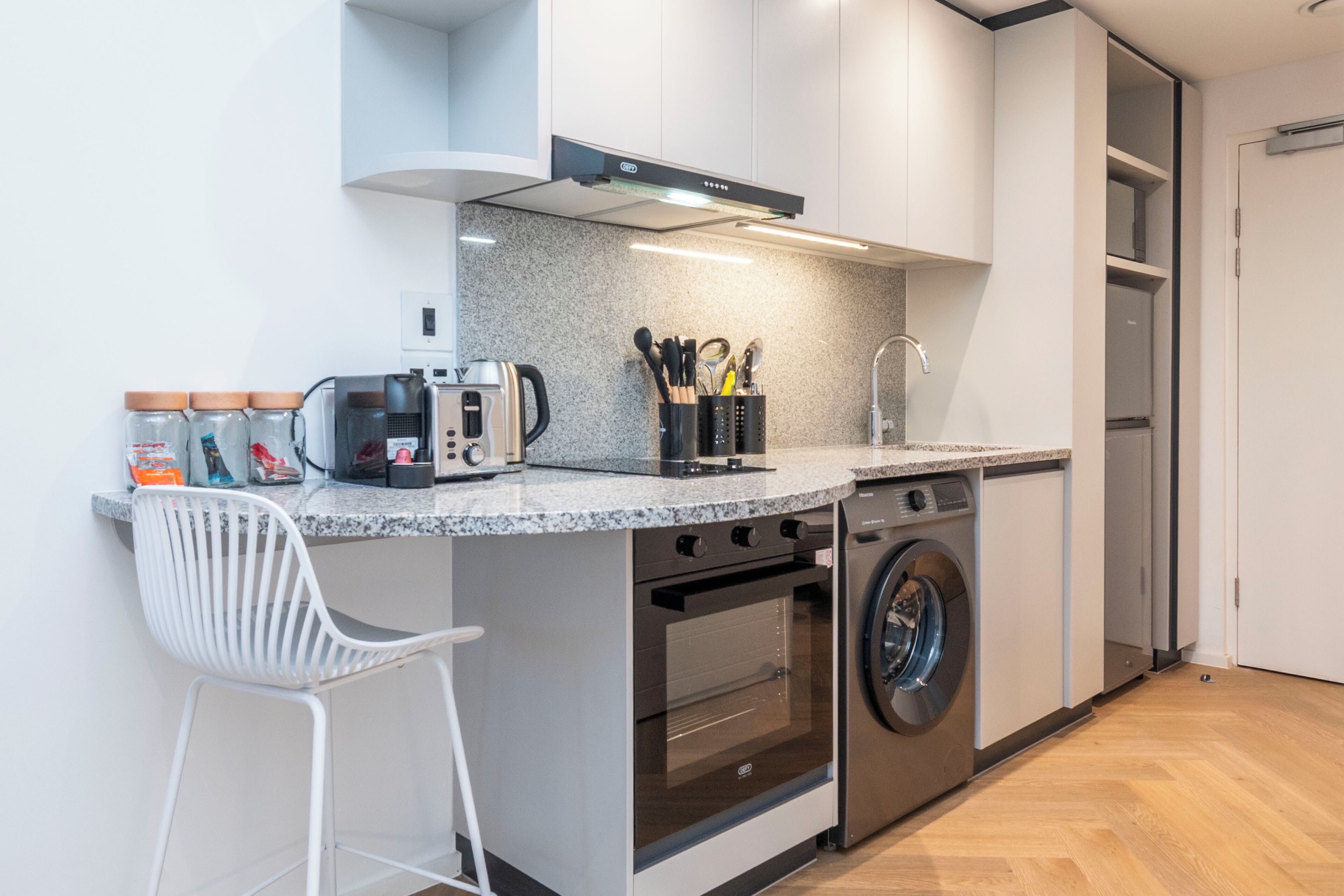 A compact kitchen with a built-in oven, a washing machine, and a coffee maker.