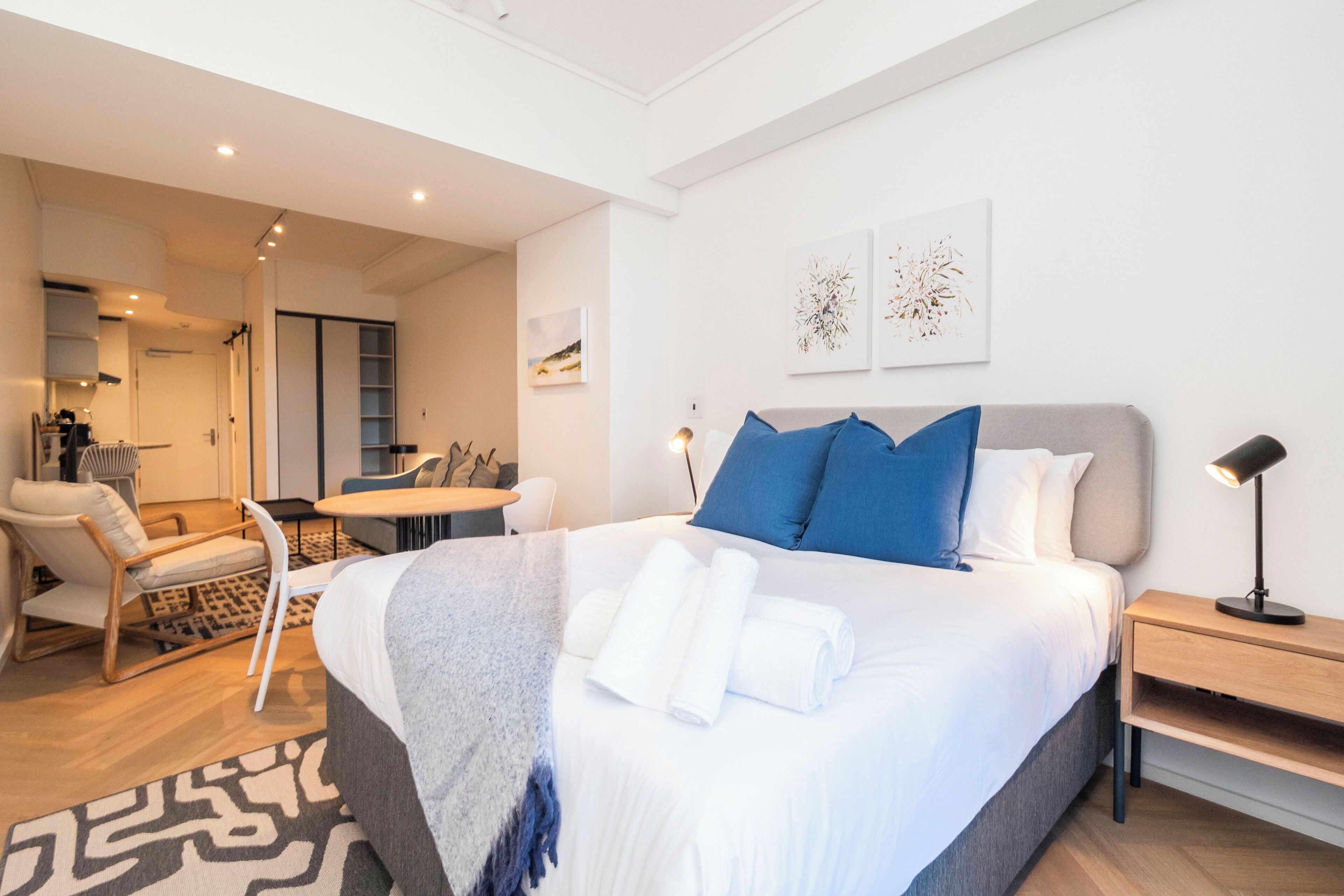 A modern hotel room with a large bed, a desk, a chair, and a small table.