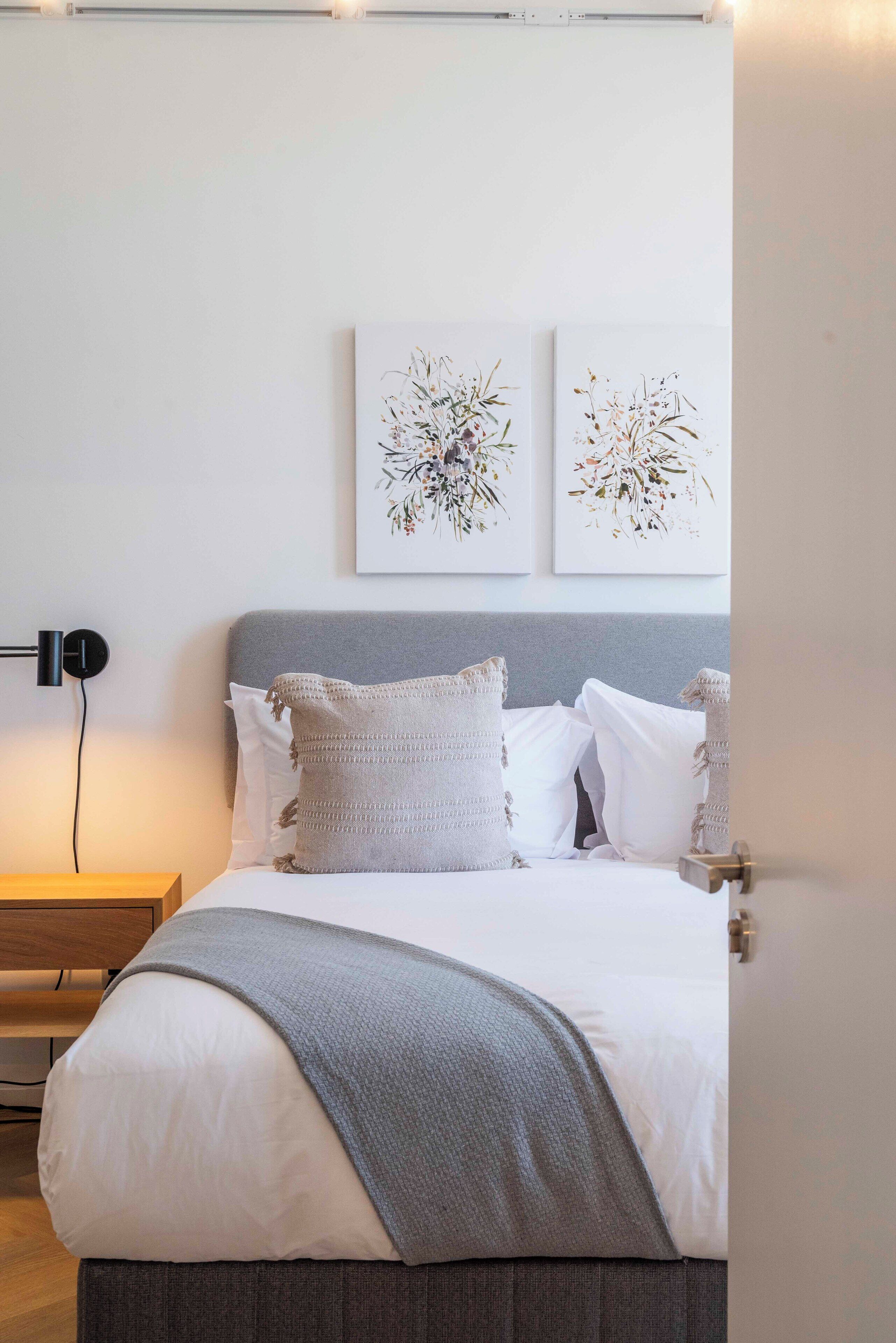 A neatly made bed with a gray blanket, white pillows, and two wall-mounted floral art pieces.