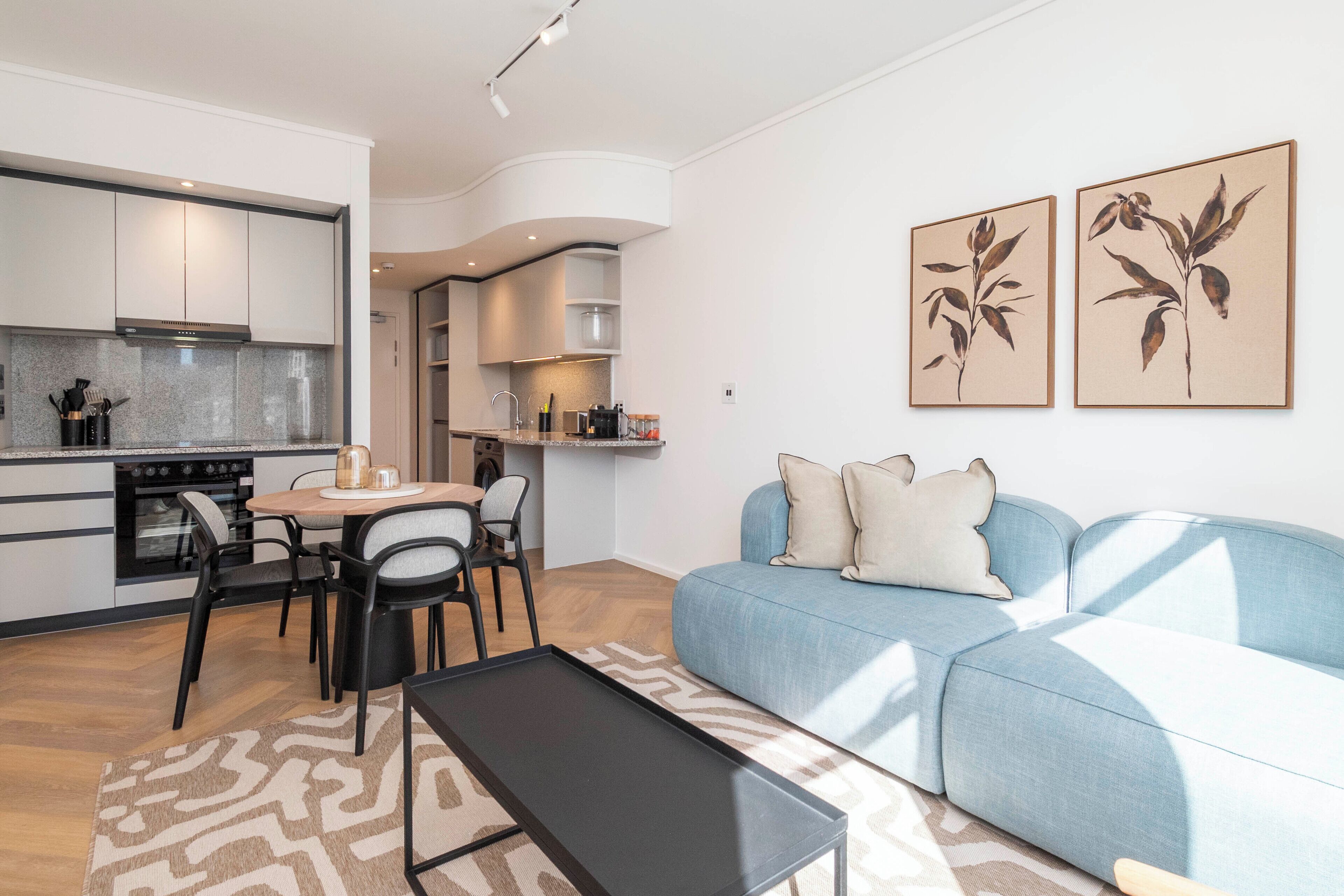 Una sala de estar moderna con un sofá azul, una mesa de comedor con sillas y una cocina con armarios y estufa.