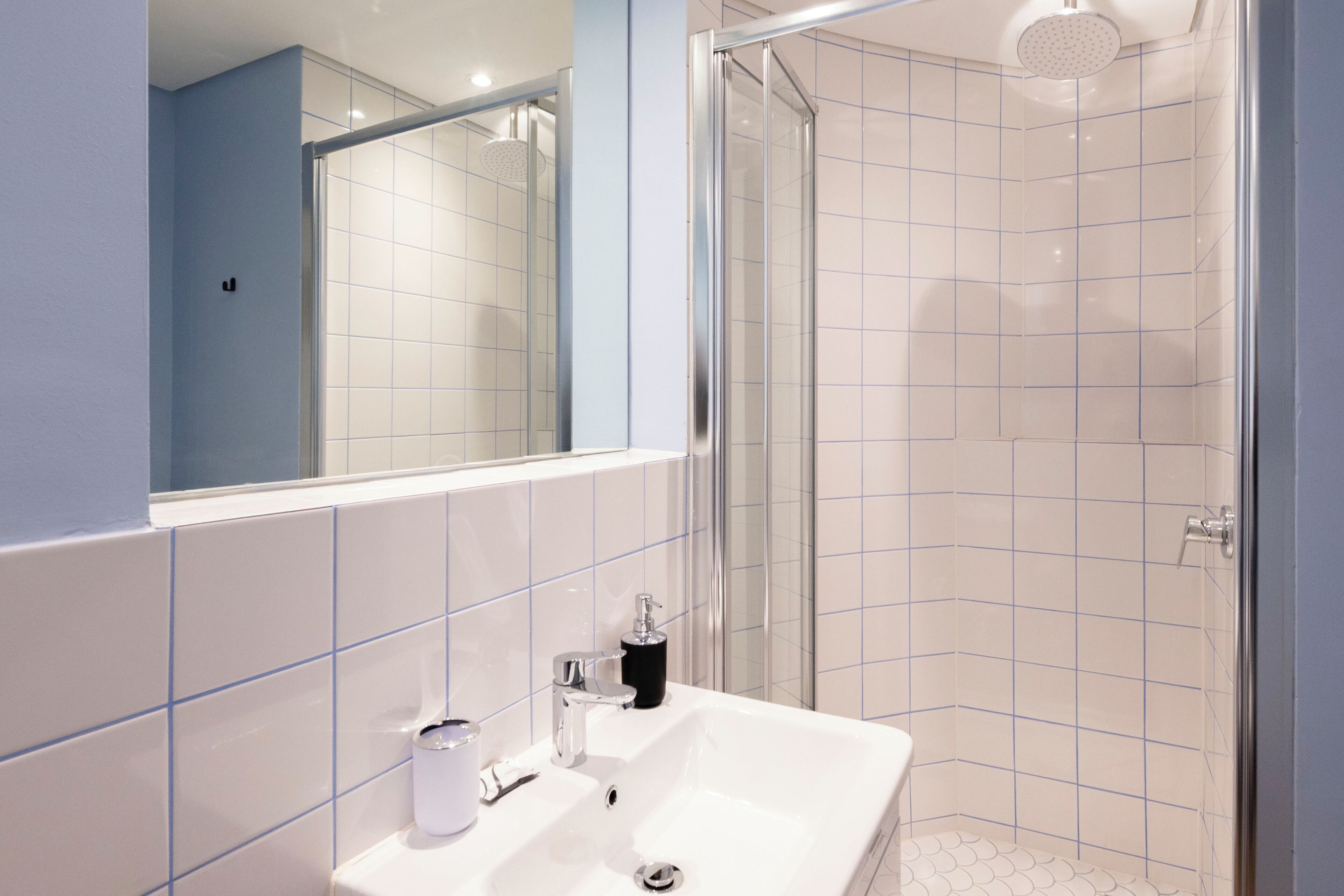 A modern bathroom with a white sink, mirror, and tiled walls.