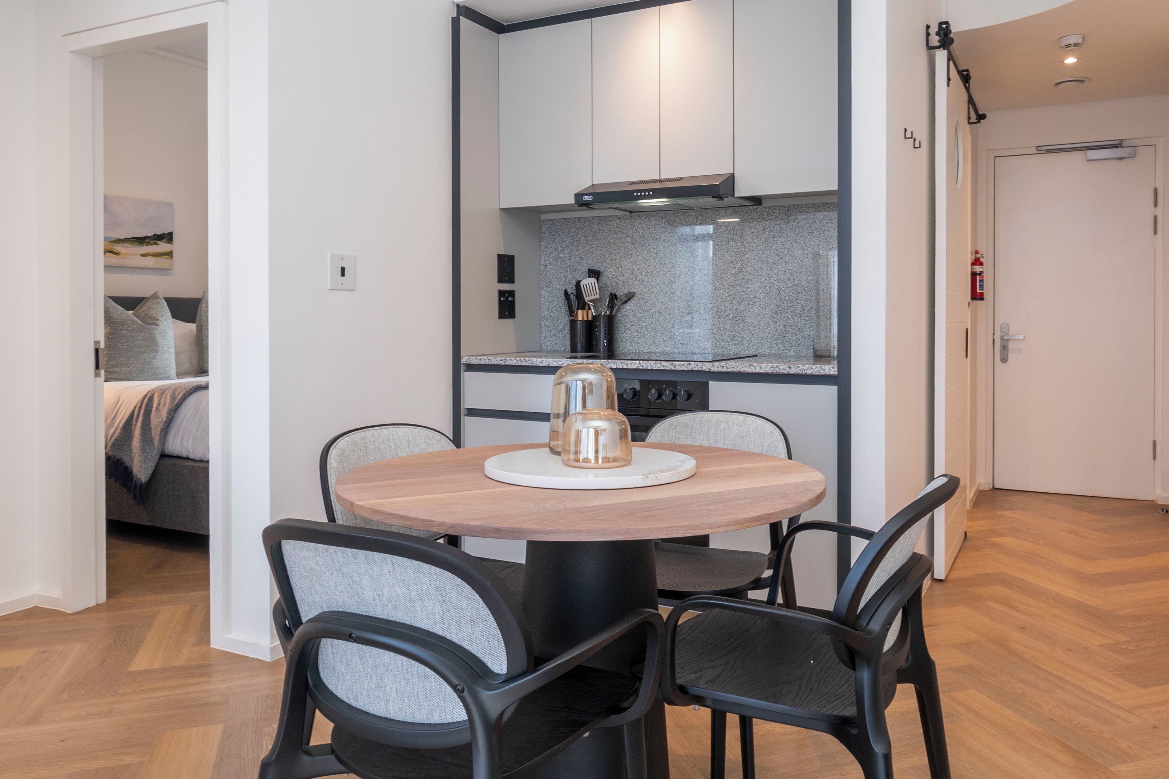 A modern kitchen with a round dining table and chairs, a built-in stove, and a small island with a coffee maker.