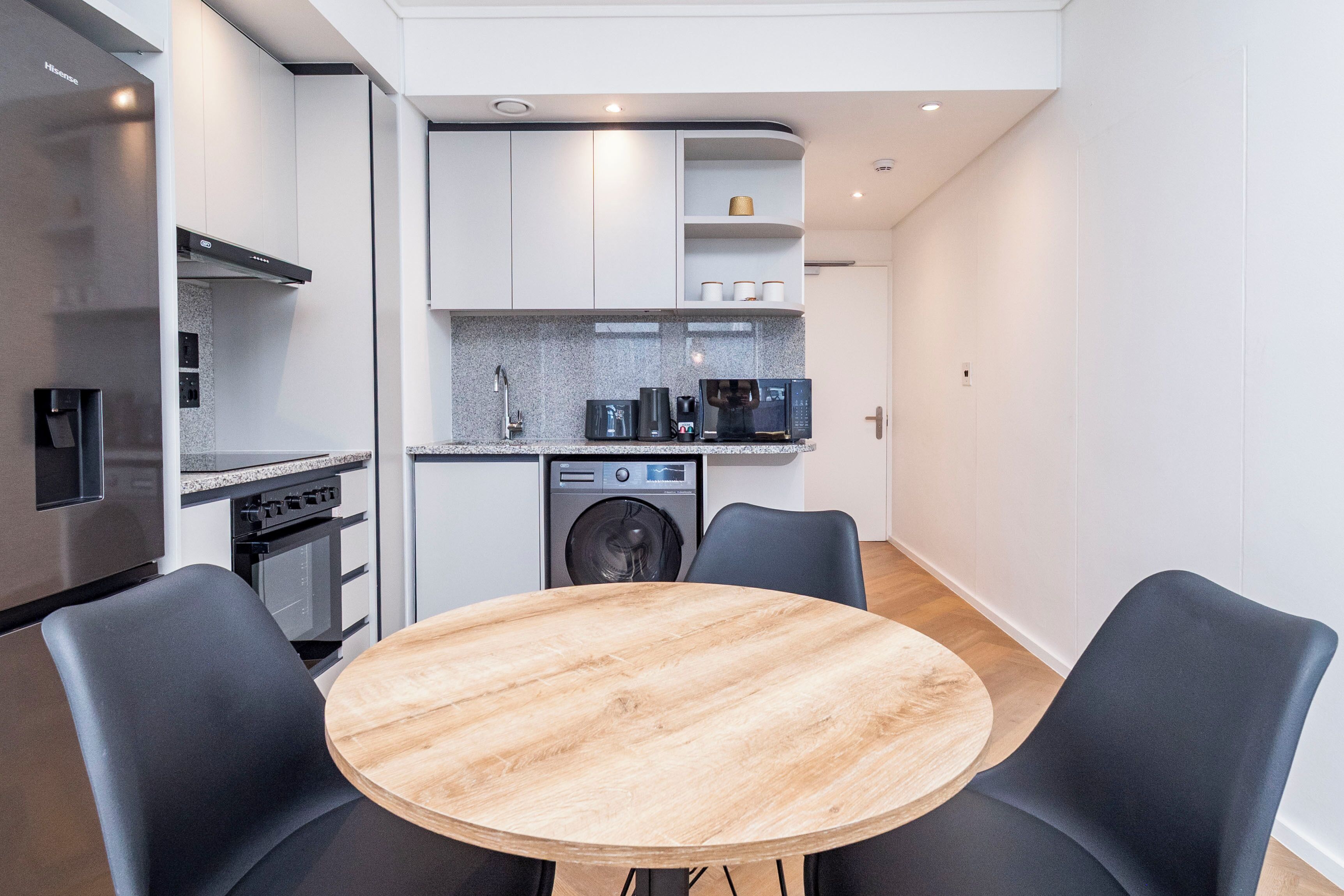 Una cucina moderna con forno a incasso, microonde e lavatrice. È presente un tavolo rotondo in legno con quattro sedie.