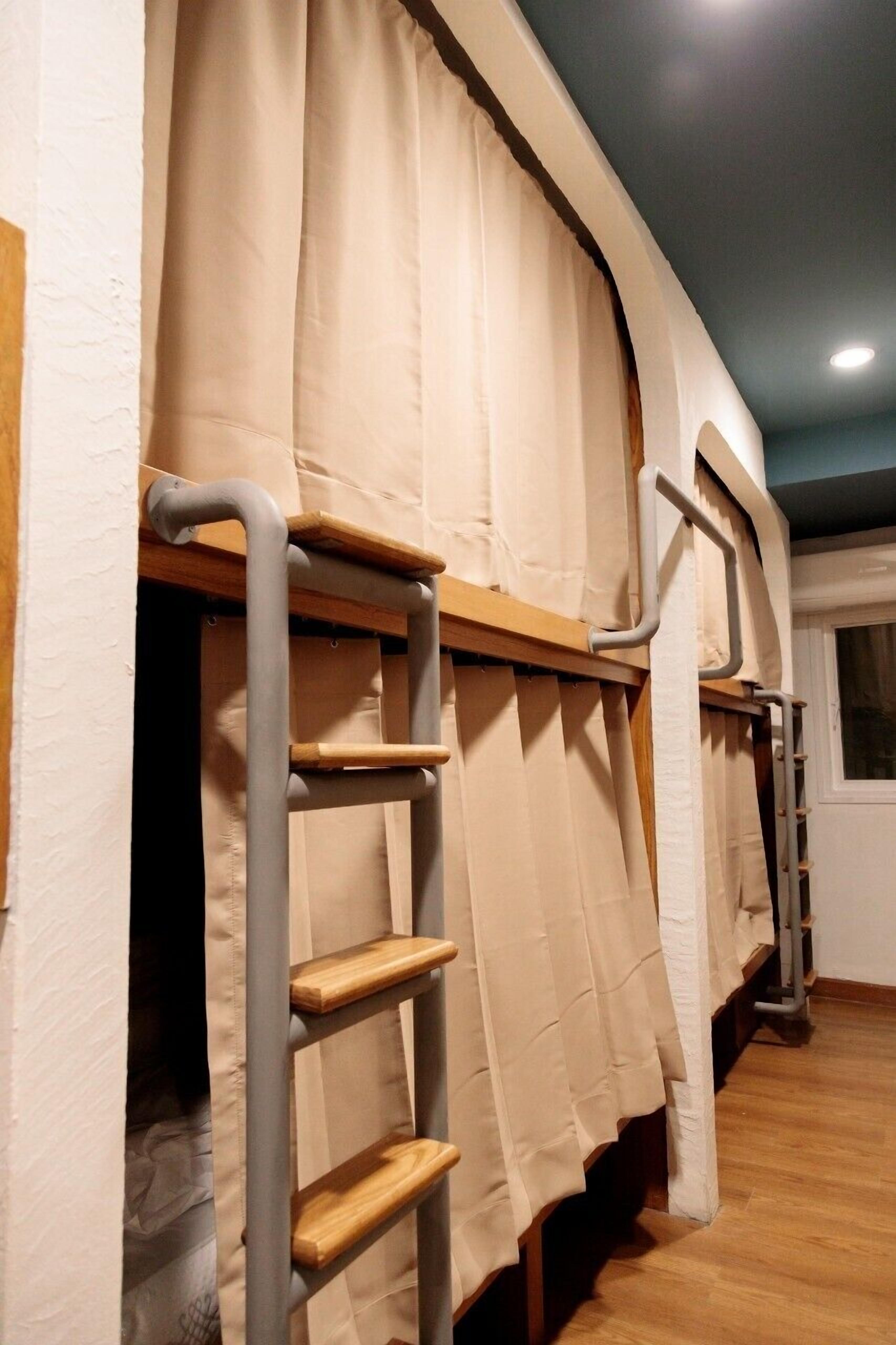 A dormitory room with bunk beds, wooden ladders, and beige curtains.
