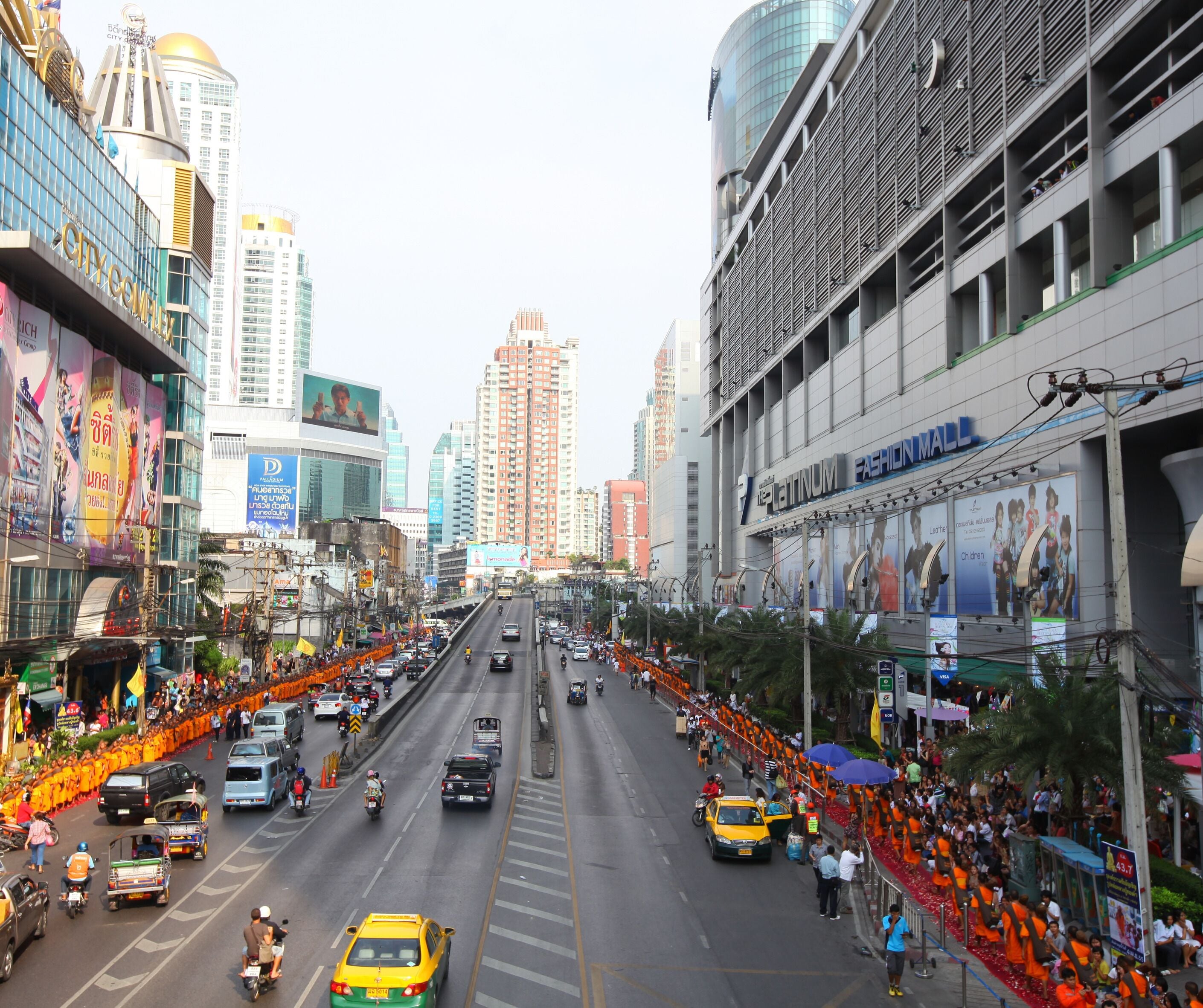 A busy urban street with a prominent fashion mall and high-rise buildings in the background.